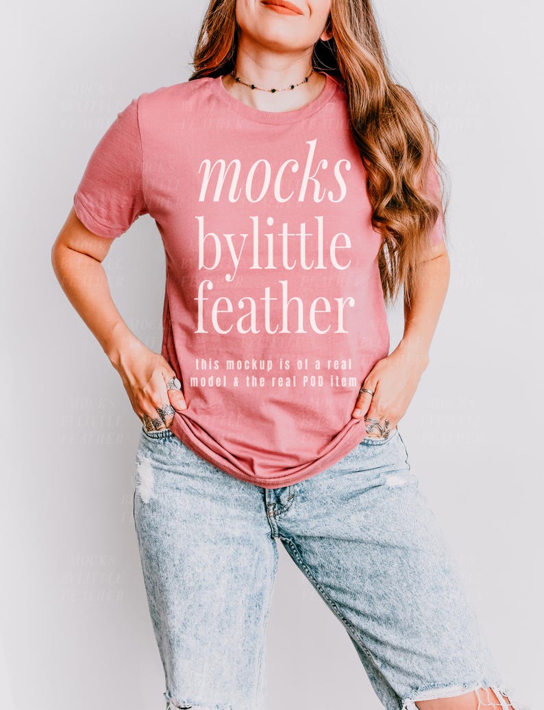 May include: A woman wearing a dusty rose t-shirt with the text "mocks bylittle feather" and the text "this mockup is of a real model & the real POD item" printed on the front. She is wearing blue jeans.
