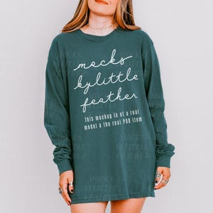 May include: A teal long-sleeved shirt with the text "mocks bylittle feather" in white lettering. The text "this mockup is of a real model & the real POD item" is also printed on the shirt.