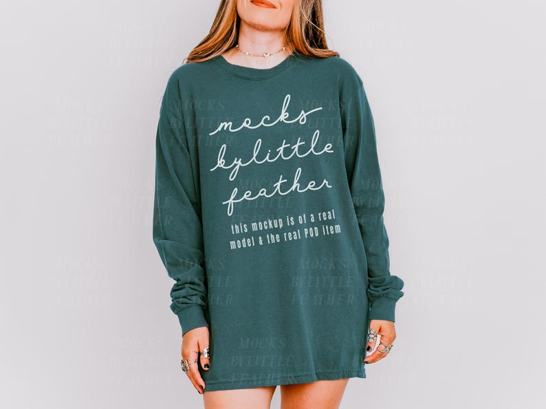 May include: A teal long-sleeved shirt with the text "mocks bylittle feather" in white lettering. The text "this mockup is of a real model & the real POD item" is also printed on the shirt.