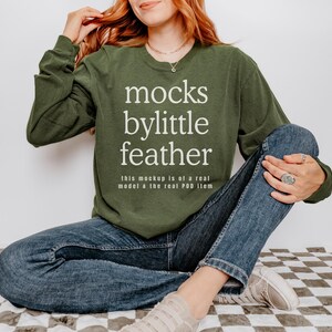 May include: A green long-sleeved sweatshirt with the text "mocks bylittle feather" and the words "this mockup is of a real model a the real POD item" printed on the front.