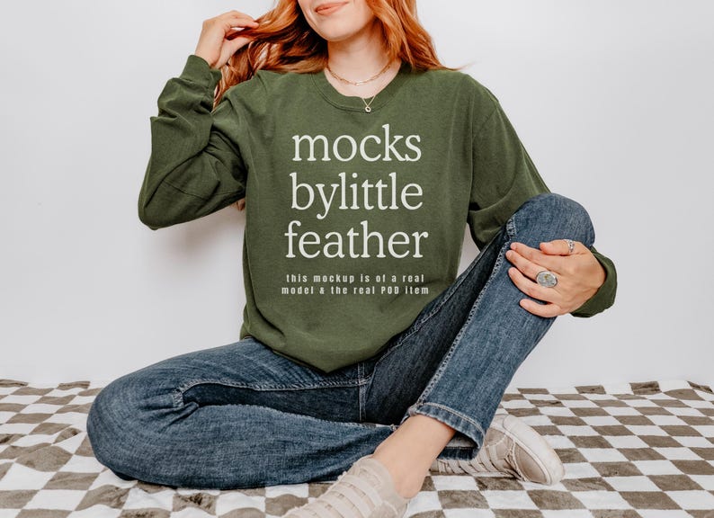 May include: A green long-sleeved sweatshirt with the text "mocks bylittle feather" and the words "this mockup is of a real model a the real POD item" printed on the front.