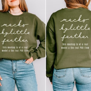 May include: An olive green long-sleeve sweatshirt featuring white text that reads "mecks by little feather" and "this mockup is of a real model & the real POD item" on the front and back, paired with blue denim jeans.