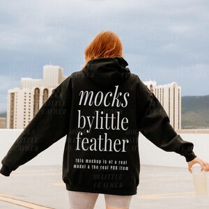 Puede incluir: Una sudadera con capucha negra con el texto "mocks bylittle feather" impreso en la espalda. El texto est&aacute; en blanco y est&aacute; centrado en la sudadera. El texto "this mockup is of a real model & the real POD item bylittle feather" est&aacute; impreso debajo del texto principal.