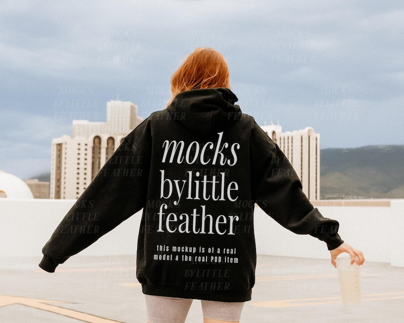 Puede incluir: Una sudadera con capucha negra con el texto "mocks bylittle feather" impreso en la espalda. El texto est&aacute; en blanco y est&aacute; centrado en la sudadera. El texto "this mockup is of a real model & the real POD item bylittle feather" est&aacute; impreso debajo del texto principal.