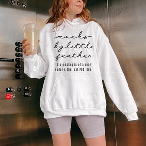 Puede incluir: Sudadera blanca de cuello alto con el texto "macks kylittle feather this mockup is of a real model & the real POD item" impreso en la parte delantera.