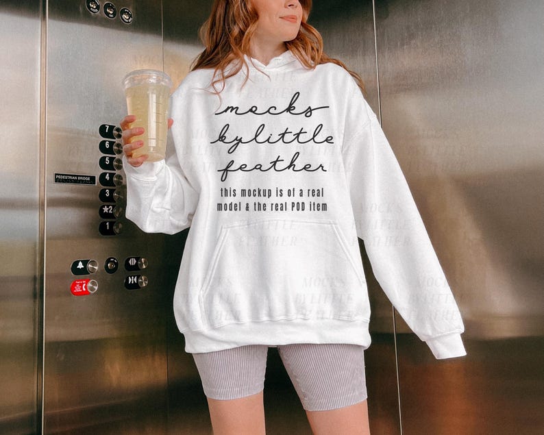 Puede incluir: Sudadera blanca de cuello alto con el texto "macks kylittle feather this mockup is of a real model & the real POD item" impreso en la parte delantera.