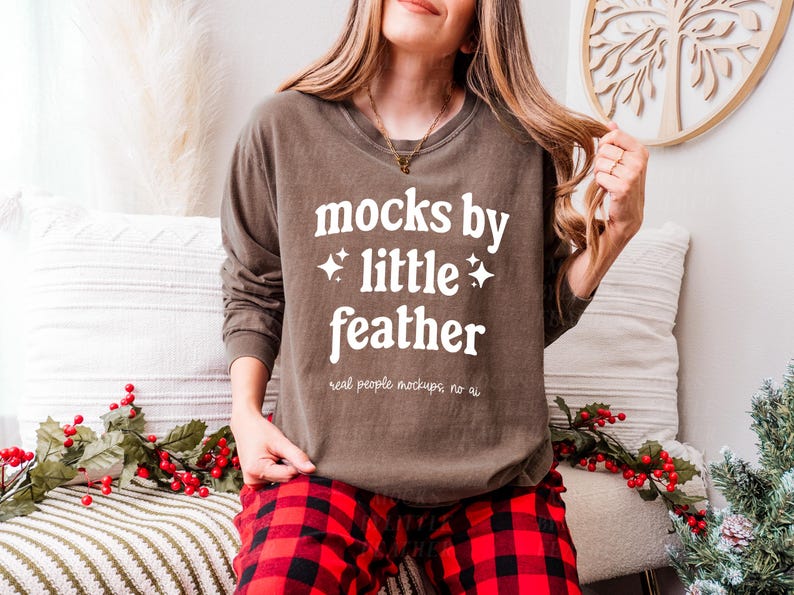 May include: A brown long-sleeved shirt with the text "mocks by little feather" and the words "real people mockups, no ai" printed on the front. The shirt is being worn by a person with long brown hair and red and black checked trousers.