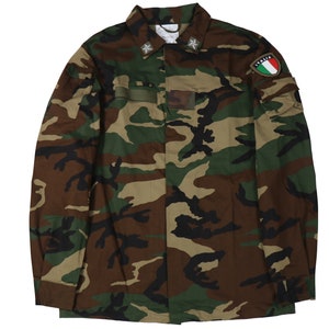 May include: A camouflage military jacket with a green, brown, and black pattern. The jacket has a button-up front, long sleeves, and two pockets on the chest. The jacket has a patch on the left sleeve that says "ITALIA".