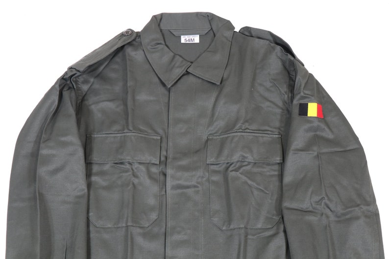 K&ouml;nnte beinhalten: Eine gr&uuml;ne Milit&auml;rjacke mit einem belgischen Flaggen-Patch am &Auml;rmel. Die Jacke hat zwei gro&szlig;e Taschen auf der Vorderseite und einen Knopfverschluss. Das Etikett am Kragen lautet "54M".