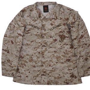 Puede incluir: Una camisa de uniforme militar de camuflaje marr&oacute;n y beige con el texto "U.S. Marines" y "LANCASTER" en la parte delantera.