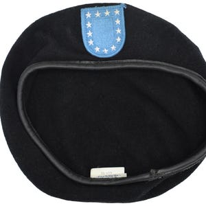 Puede incluir: Boina negra con un parche del ejército de los Estados Unidos en azul y blanco. La boina tiene una banda de cuero negro en el interior.