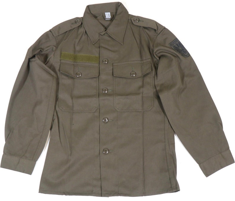 K&ouml;nnte beinhalten: Ein lang&auml;rmeliges, olivgr&uuml;nes Hemd im Milit&auml;rstil mit Knopfleiste und zwei Pattentaschen. Das Hemd hat einen Aufn&auml;her auf dem rechten &Auml;rmel mit einem schwarzen Adler.