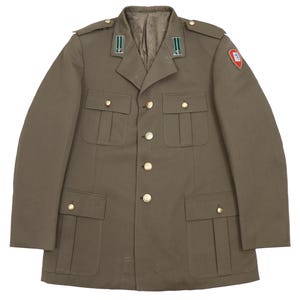 Könnte beinhalten: Olivgrüne Militärjacke mit goldenen Knöpfen und vier Vordertaschen. Die Jacke hat Schulterklappen und einen Aufnäher am oberen linken Ärmel. Der Kragen hat grün-weiße Streifen.