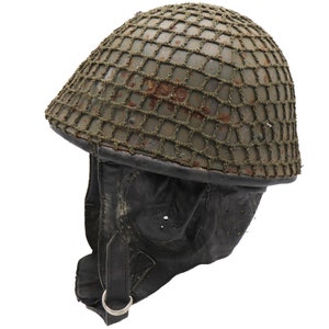 May include: A green military helmet with a camouflage net. The helmet has a black leather chin strap with a metal ring.