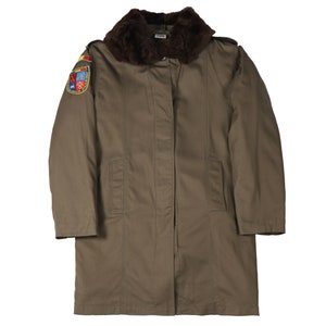 May include: A long, brown, military-style coat with a fur collar and a patch on the left sleeve. The patch features a colorful design with a shield and other symbols.