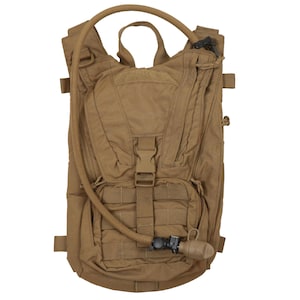 Puede incluir: Una mochila de hidratación de color marrón claro con un tubo de hidratación y una válvula de mordida. La mochila tiene múltiples correas y bolsillos.