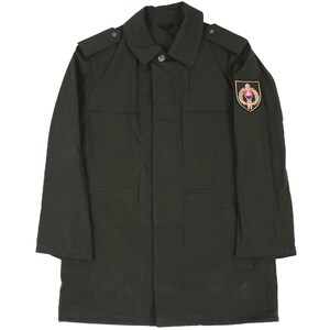 May include: A dark green military-style jacket with a patch on the right sleeve featuring a gold emblem with a red and white design.