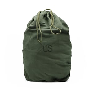 May include: An olive green canvas drawstring bag featuring the letters US printed in black on the front. The bag has a gathered top closure secured with matching olive green fabric cords that are tied together at the top center of the bag.