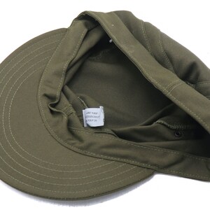 K&ouml;nnte beinhalten: Eine gr&uuml;ne Milit&auml;rkappe mit einem umklappbaren Klappenteil. Die Kappe hat ein Etikett mit der Aufschrift "Made in Korea, 100% Baumwolle, Gr&ouml;&szlig;e 57".