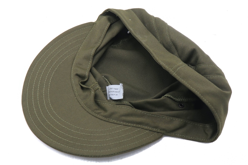 K&ouml;nnte beinhalten: Eine gr&uuml;ne Milit&auml;rkappe mit einem umklappbaren Klappenteil. Die Kappe hat ein Etikett mit der Aufschrift "Made in Korea, 100% Baumwolle, Gr&ouml;&szlig;e 57".