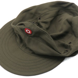 K&ouml;nnte beinhalten: Eine gr&uuml;ne Milit&auml;rkappe mit einem roten und wei&szlig;en runden Emblem auf der Vorderseite. Die Kappe hat einen Schirm und einen Knopf oben.