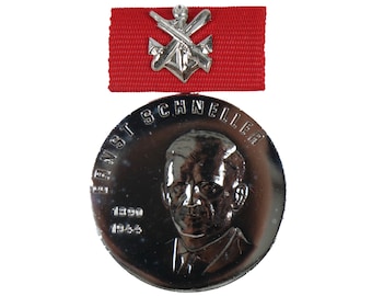 May include: A silver medal with a portrait of Ernst Schneller and the text "Ernst Schneller 1900-1964". The medal is attached to a red ribbon with a silver emblem.