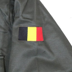 K&ouml;nnte beinhalten: Eine gr&uuml;ne Milit&auml;rjacke mit einem schwarzen, gelben und roten Aufn&auml;her am &Auml;rmel. Der Aufn&auml;her ist die Flagge Belgiens.