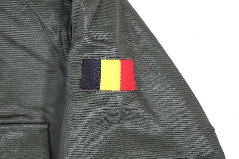 K&ouml;nnte beinhalten: Eine gr&uuml;ne Milit&auml;rjacke mit einem schwarzen, gelben und roten Aufn&auml;her am &Auml;rmel. Der Aufn&auml;her ist die Flagge Belgiens.