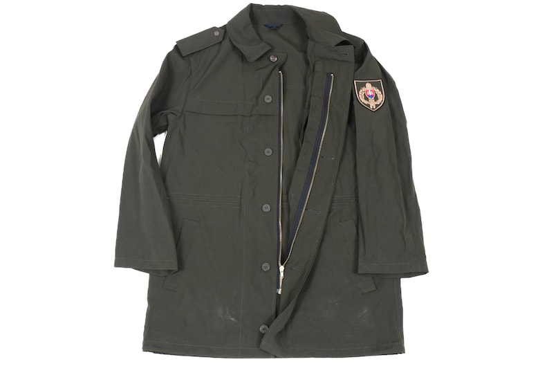 May include: A dark green military-style jacket with a zipper and button closure. The jacket has a patch on the right shoulder with a gold emblem.