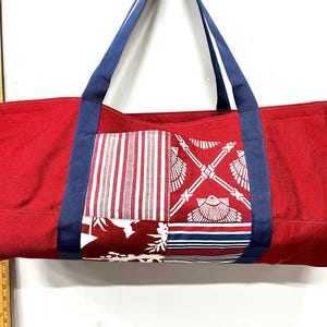 May include: A red rectangular tote bag with blue handles and a patchwork front panel featuring white stripes, shell motifs, and floral patterns. A yellow wooden ruler is visible on the left, showing a height of approximately 12 inches.