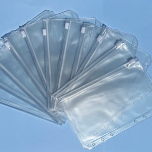 May include: A set of ten clear plastic zippered pouches with holes for a binder. The pouches are arranged in a fan shape.
