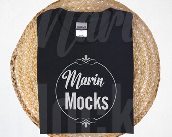May include: Black t-shirt with a white circle design that says "Marin Mocks" on a woven straw background.