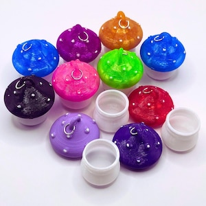 May include: A collection of colorful, mushroom-shaped containers with small, white dots and silver hoops. The mushrooms come in various colors, including blue, purple, orange, green, pink, black, and red. Several white, cylindrical containers are also present.