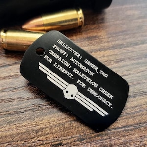 May include: Black dog tag with white text and a skull graphic. The tag reads "HELLDIVER: GAMER_TAG FRONT: AUTOMATON CAMPAIGN: MALEVELON CREEK FOR LIBERTY. FOR DEMOCRACY." Gold-colored bullets are in the background.