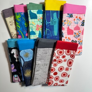 May include: A collection of 10 fabric swatches with different patterns and colors. The swatches are folded in half and have a contrasting colored trim. The patterns include geometric shapes, animals, and floral designs.