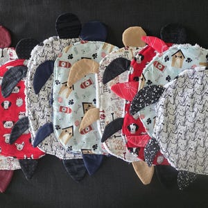May include: A collection of seven fabric turtle-shaped ornaments featuring various patterns including red with dog faces, light blue with dog houses, and white with black cat outlines. Each turtle has a round body and four protruding fabric flippers.