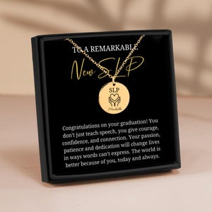 May include: A gold necklace in a black box with a round pendant that says "SLP" with a heart and hands. The box has a message that says "To a remarkable new SLP. Congratulations on your graduation! You don't just teach speech, you give courage, confidence, and connection. Your passion, patience and dedication will change lives in ways words can't express. The world is better because of you, today and always."