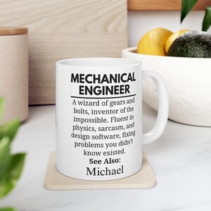 May include: White ceramic mug with a black inscription that reads "MECHANICAL ENGINEER. A wizard of gears and bolts, inventor of the impossible. Fluent in physics, sarcasm, and design software, fixing problems you didn't know existed. See Also: Michael"