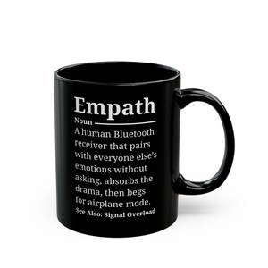 May include: A black ceramic mug featuring white text that defines the word Empath as a human Bluetooth receiver that pairs with everyone else's emotions without asking, absorbs the drama, then begs for airplane mode. See Also: Signal Overload.