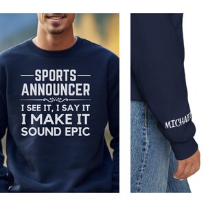 May include: Navy blue sweatshirt with white text that reads "SPORTS ANNOUNCER I SEE IT, I SAY IT I MAKE IT SOUND EPIC." The sleeve has the name "MICHAEL" printed in white. The sweatshirt is a crew neck style.