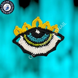 May include: A crocheted eye design with a black centre, white and green stripes, and a yellow crown. The eye is crocheted in a 3D style and has a textured surface.