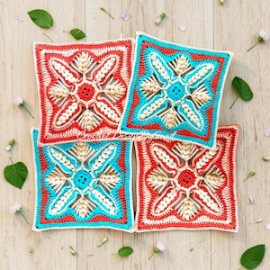 Op de afbeelding: Vier gehaakte vierkanten in rood, turquoise en beige liggen op een houten oppervlak. Elk vierkant heeft een centraal bloemmotief met een rood midden, omgeven door beige en witte details. De vierkanten worden omlijst door turquoise en rode randen.
