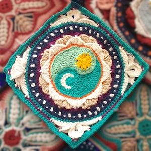 May include: A square, handmade crochet doily featuring a central yin-yang design in teal, green, and yellow. The doily has a teal border and is surrounded by concentric circles of various colors and textures, including white, beige, and purple.