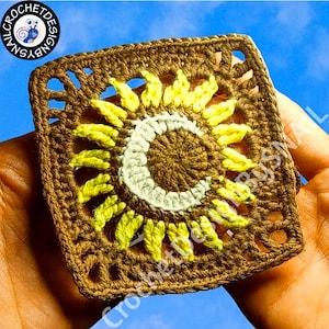 Pode incluir: Um quadrado de crochê marrom com um design de girassol amarelo e branco no centro.