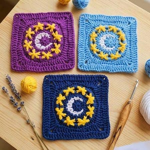 May include: Three crocheted square coasters in purple, blue, and navy blue. Each coaster features a crescent moon and star design in yellow and white. The coasters are handmade and sit on a wooden surface.