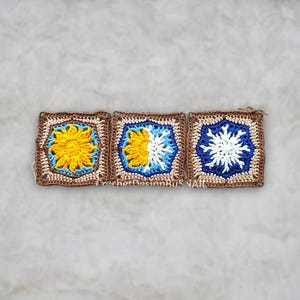 May include: Three handmade crochet squares with floral designs. The squares feature a brown border, with yellow, white, and blue accents. The center of each square has a different design, including a sun and a snowflake. The squares are displayed on a neutral background.