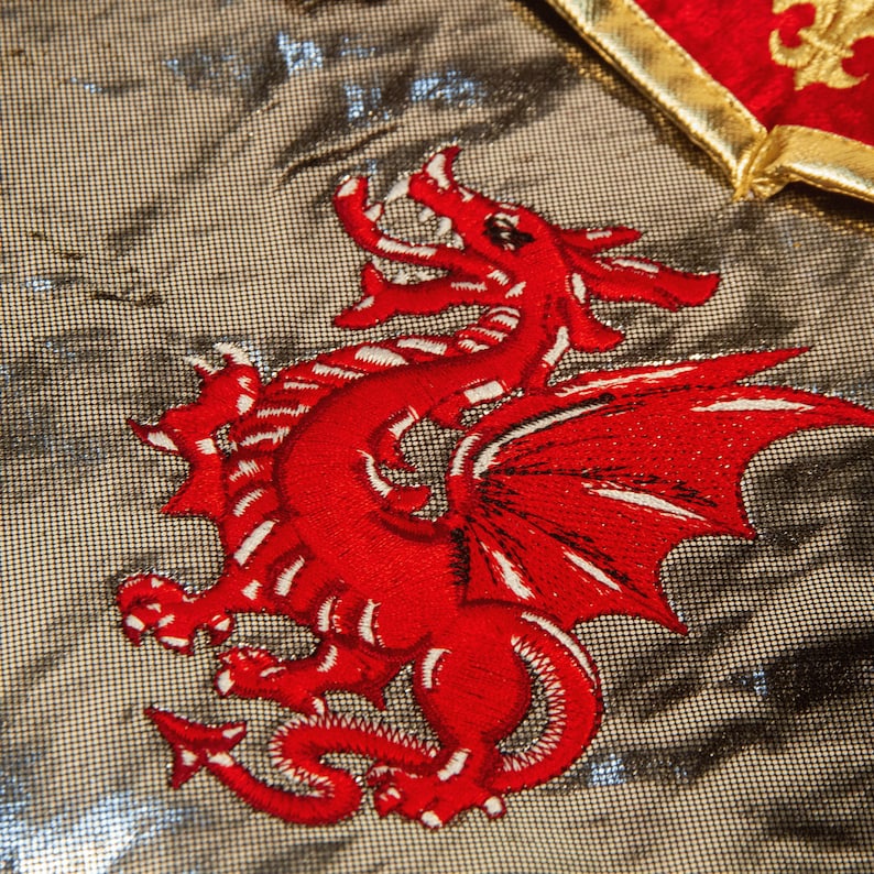May include: A red embroidered dragon with white accents on a silver background. The dragon is facing right and has its wings spread out.
