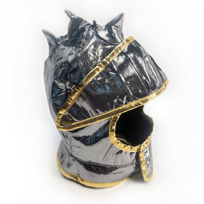 May include: A silver and gold knight helmet costume for kids. The helmet has a pointed top and a face mask with a small opening for the eyes.