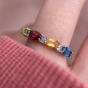 Puede incluir: Un anillo de plata con una fila de piedras preciosas ovaladas en verde, rojo, amarillo y azul.