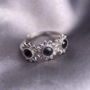 May include: A silver ring with three black gemstones set in a sunflower design.